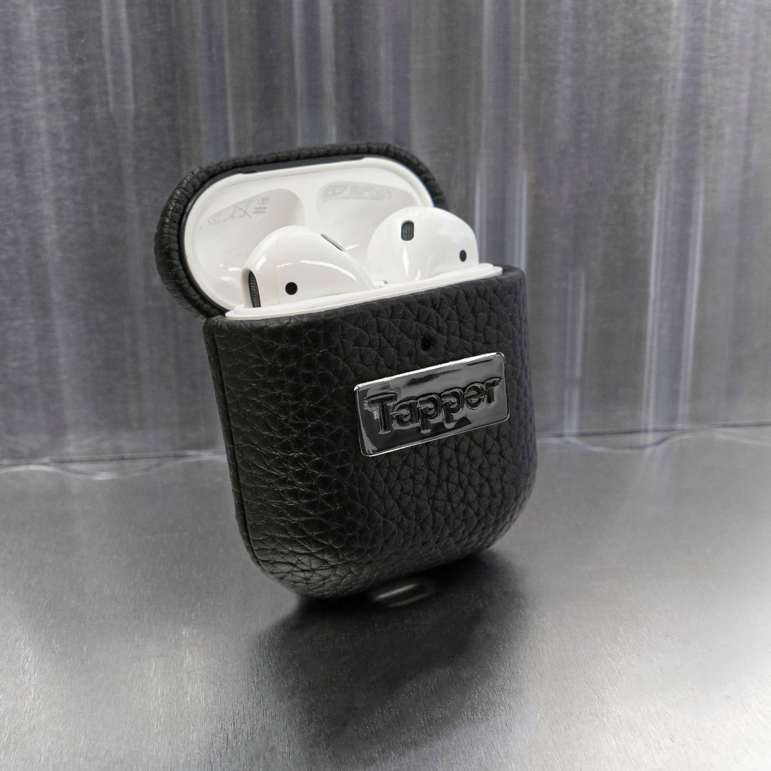 Tapper's luxurious black genuine cow leather AirPods case protects and elevates the look of your AirPods. The luxurious, protective case for AirPods with a metal logo plate in hematite black plating steps up your AirPods game. The next must-have high end protective Apple AirPods accessory in real leather and precious metals. Compatible with AirPods (1st and 2nd generation). Designed in Sweden by Tapper. Free Express Shipping at gettapper.com