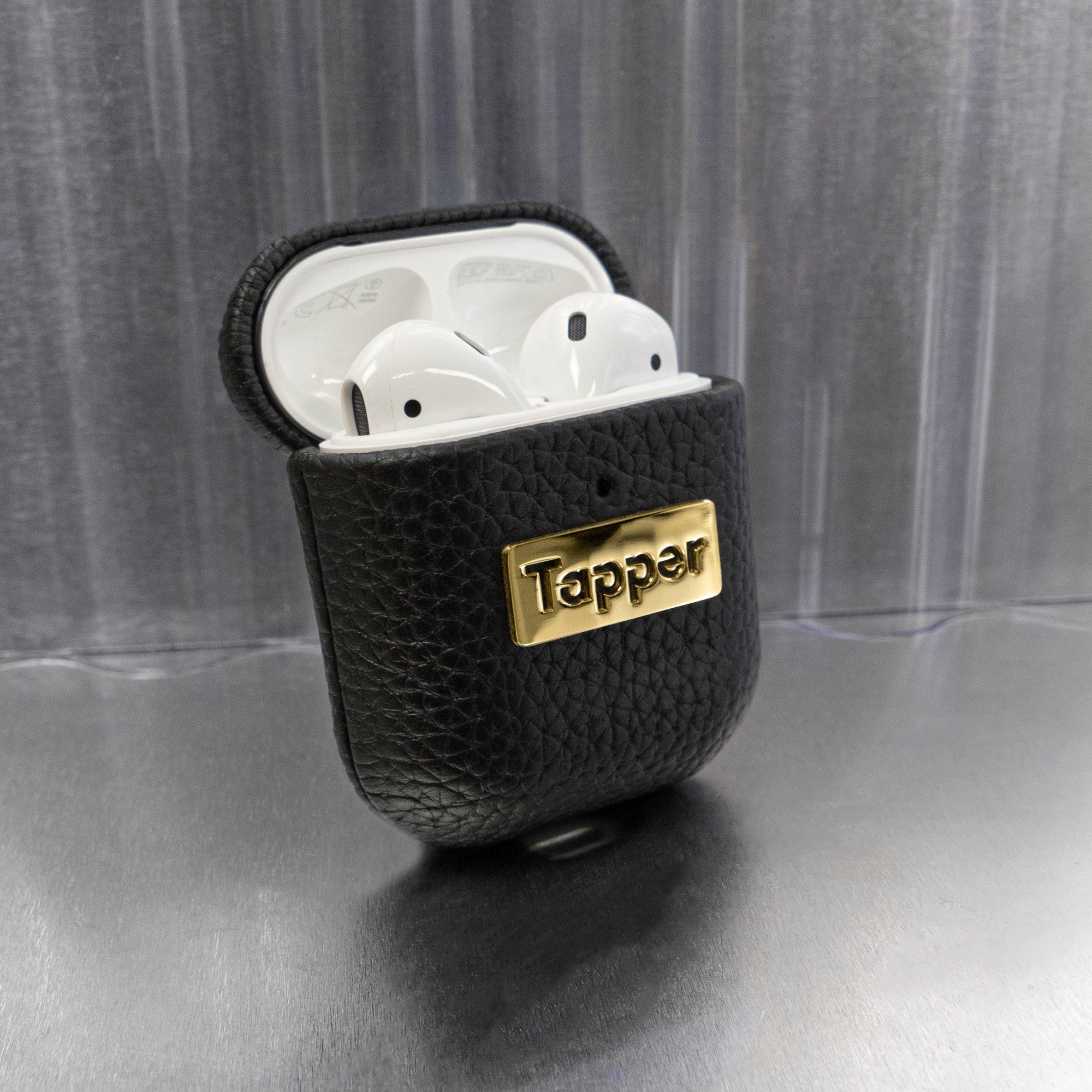 Tapper's luxurious black genuine cow leather AirPods case protects and elevates the look of your AirPods. The luxurious, protective case for AirPods with a metal logo plate in real 18k gold plating steps up your AirPods game. The next must-have high end protective Apple AirPods accessory in real leather and precious metals. Compatible with AirPods (1st and 2nd generation). Designed in Sweden by Tapper. Free Express Shipping at gettapper.com